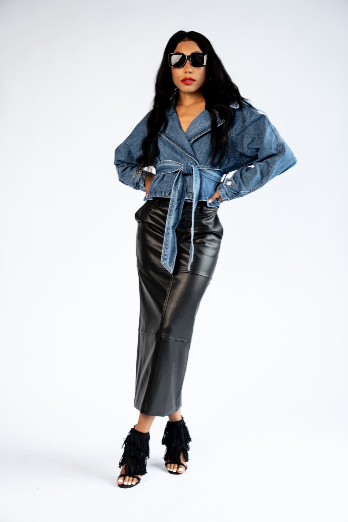 Full-length front view of a model wearing the blue cropped denim trench coat with a black faux-leather midi skirt.