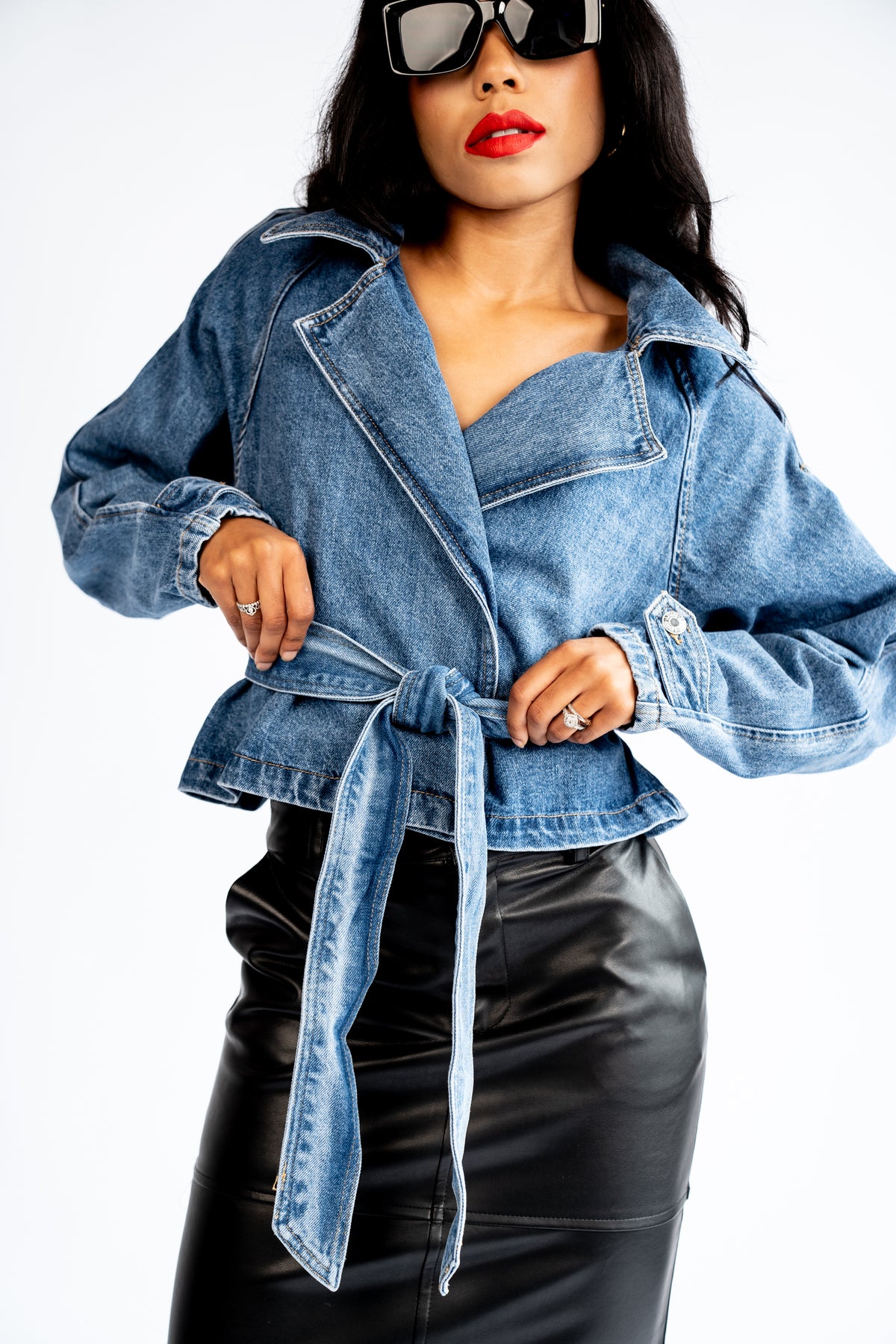 Close-up of the blue cropped denim trench coat showing the notched lapels, tied belt and flared hem.