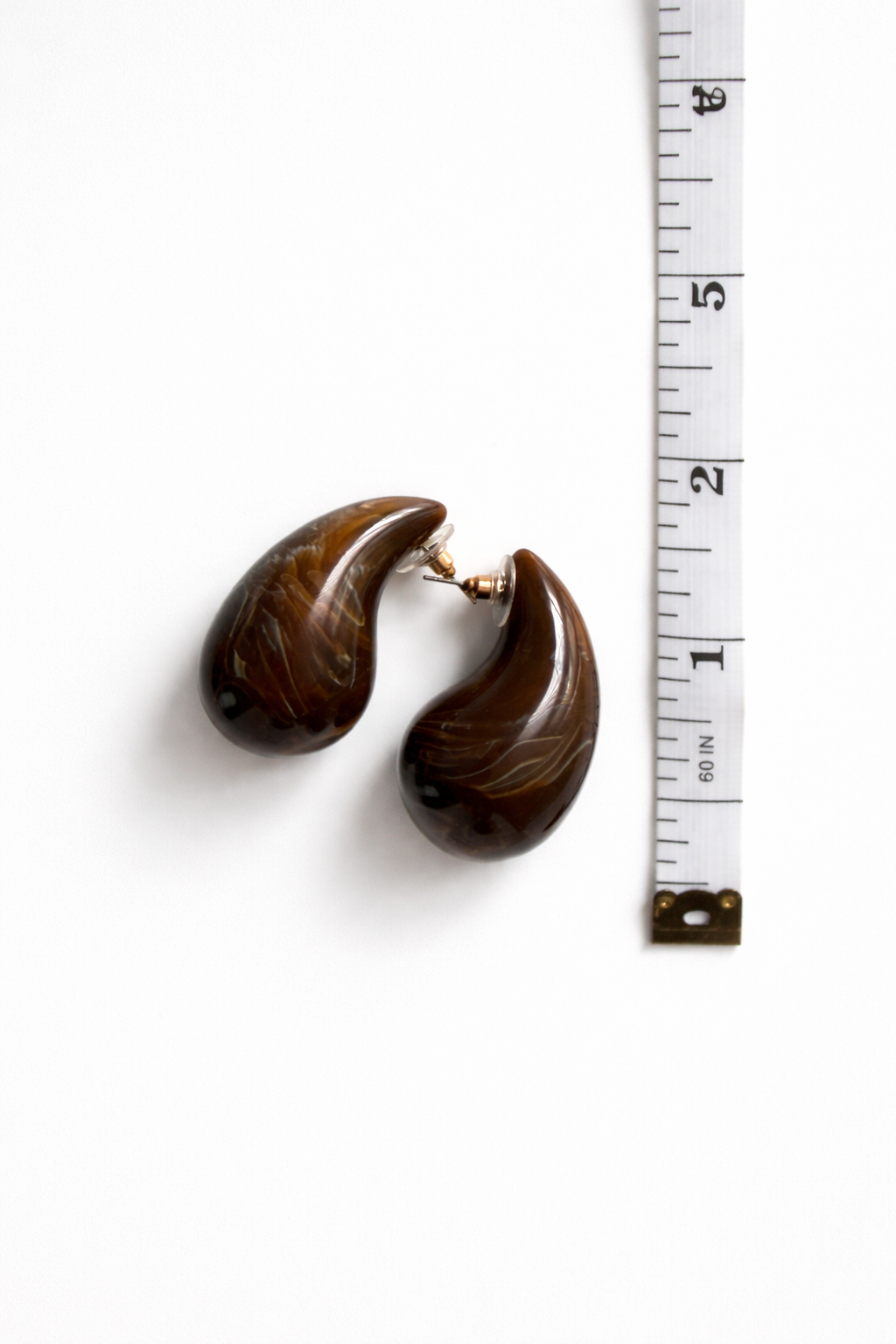 Pair of brown earrings next to a measuring tape on a white background