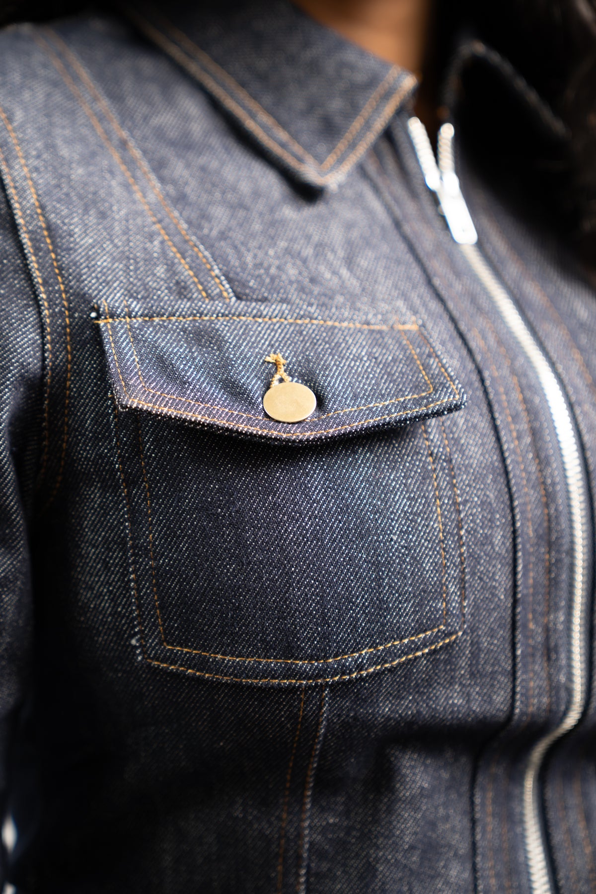 Detail view of the fitted waist and zip-front closure on the indigo denim jacket