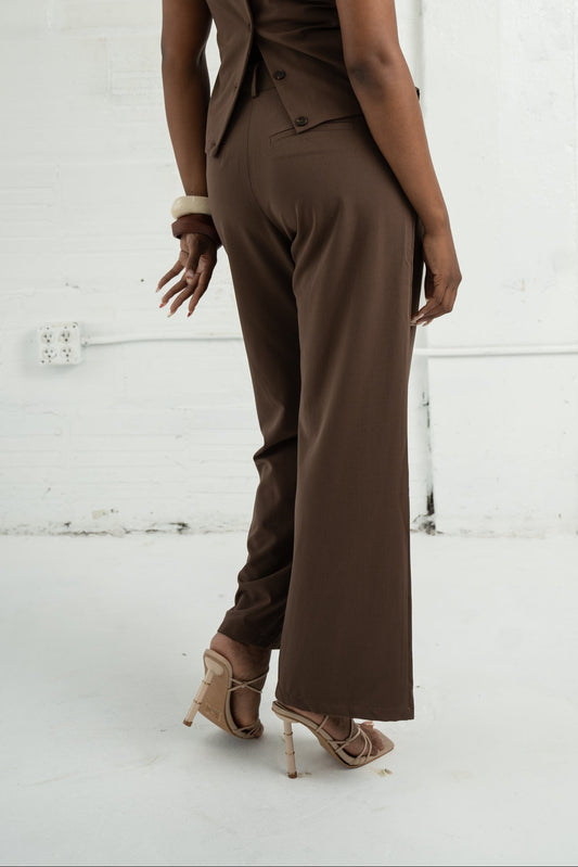 Woman wearing a brown jumpsuit against a white brick wall.