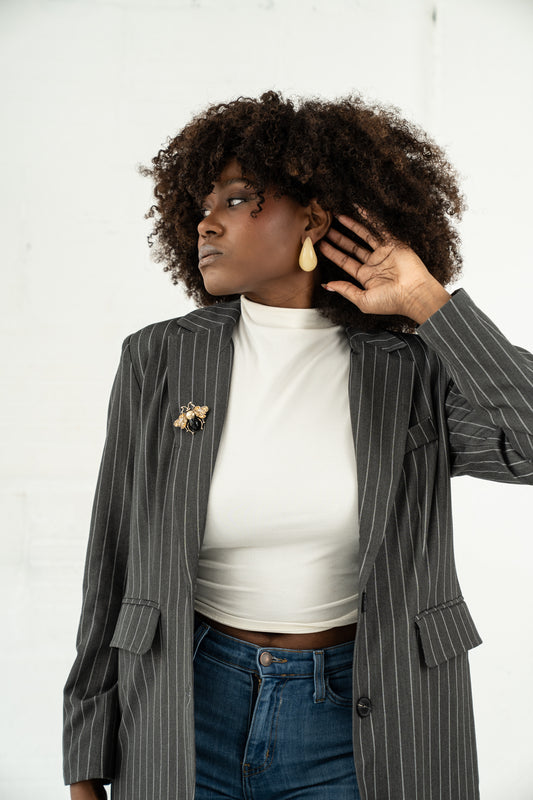Woman wearing a gray pinstripe blazer over a white top and blue jeans, with a plain background.