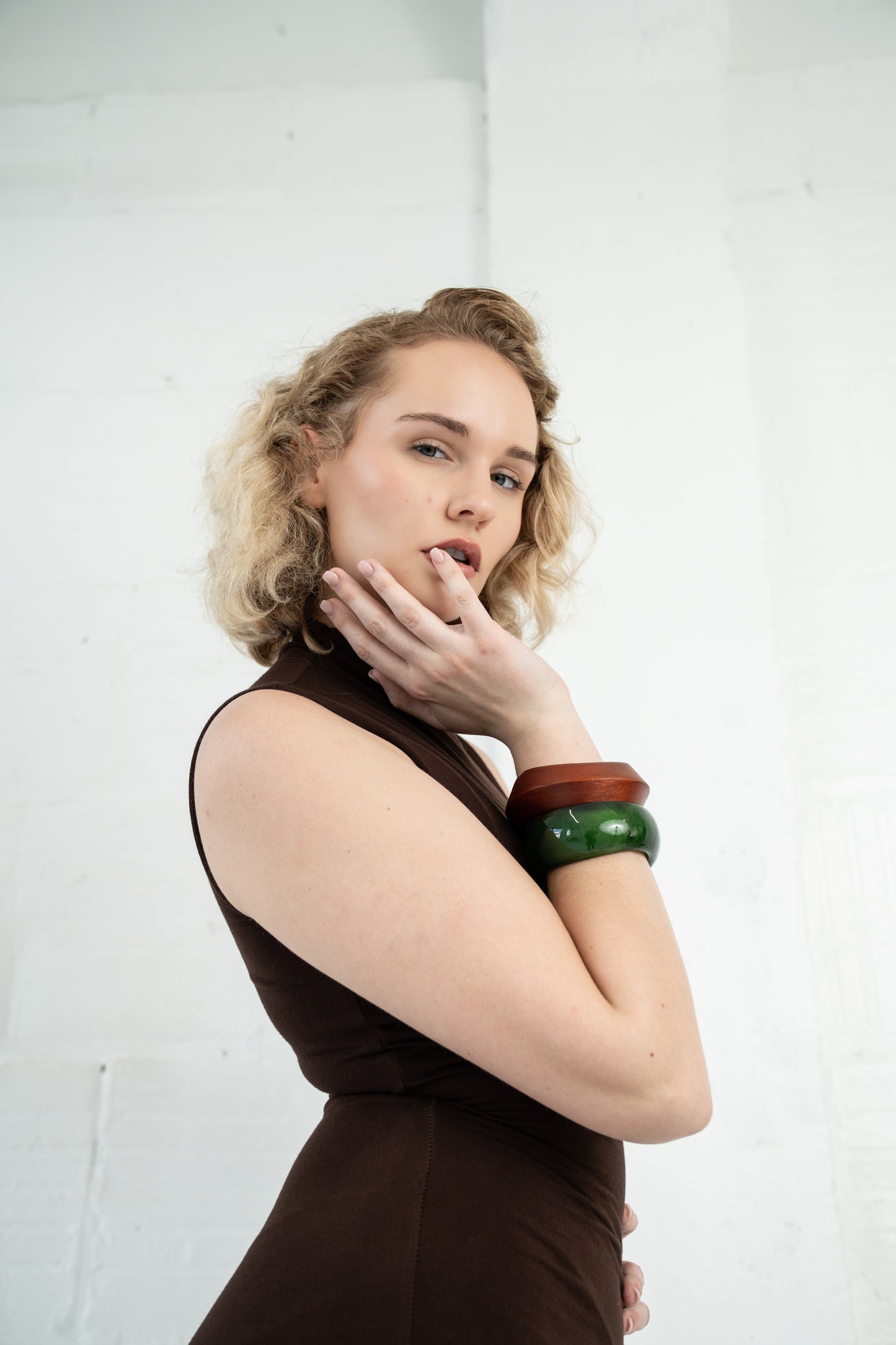 Woman wearing a brown sleeveless top and green bracelets on a white background