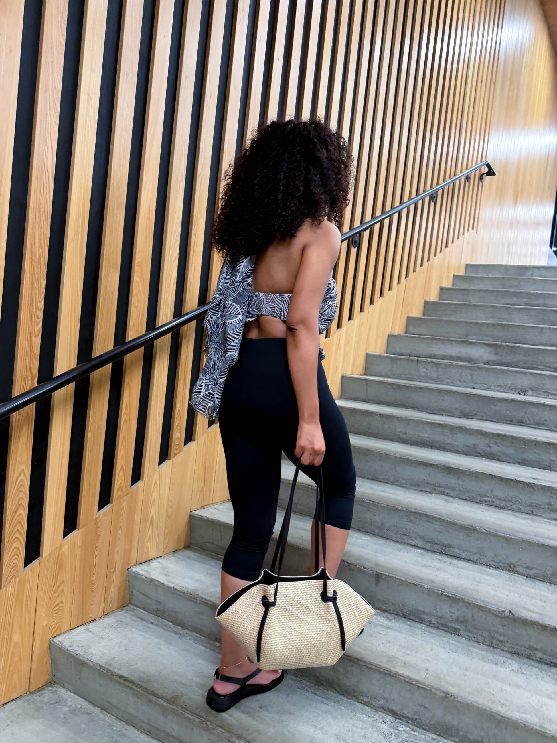 Woman with an afro standing on a staircase holding a beige handbag.