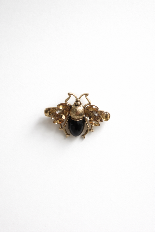 Gold bee-shaped brooch with a black center on a white background