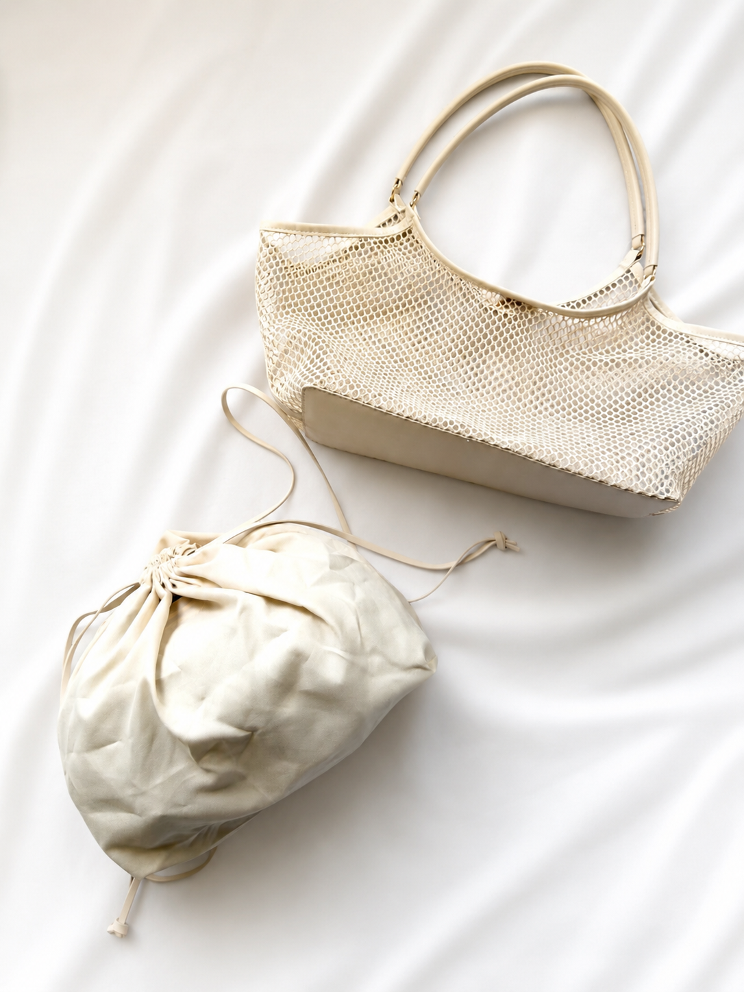 Beige handbag and drawstring bag on a white fabric background