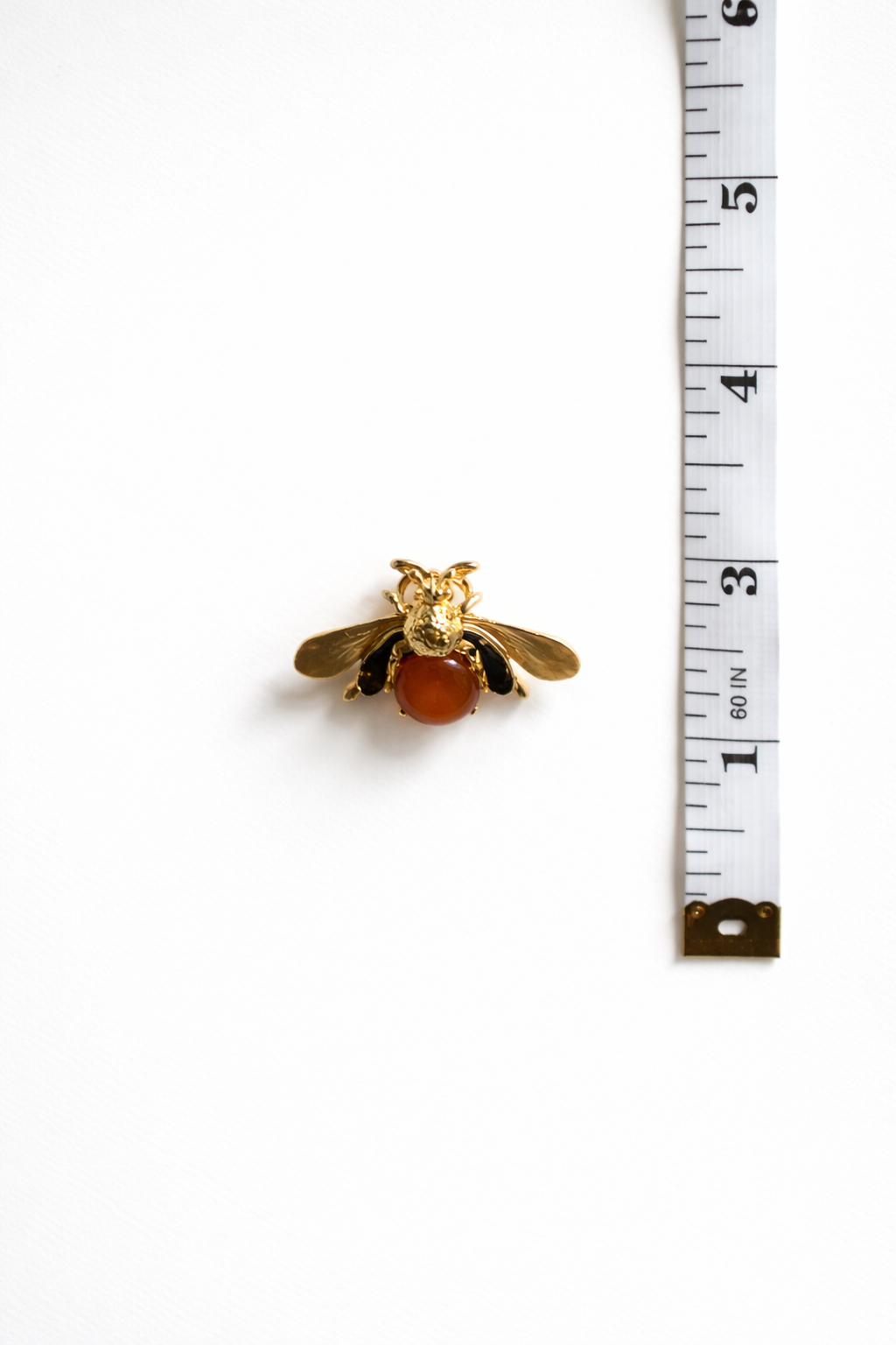 Gold bee-shaped brooch next to a ruler on a white background