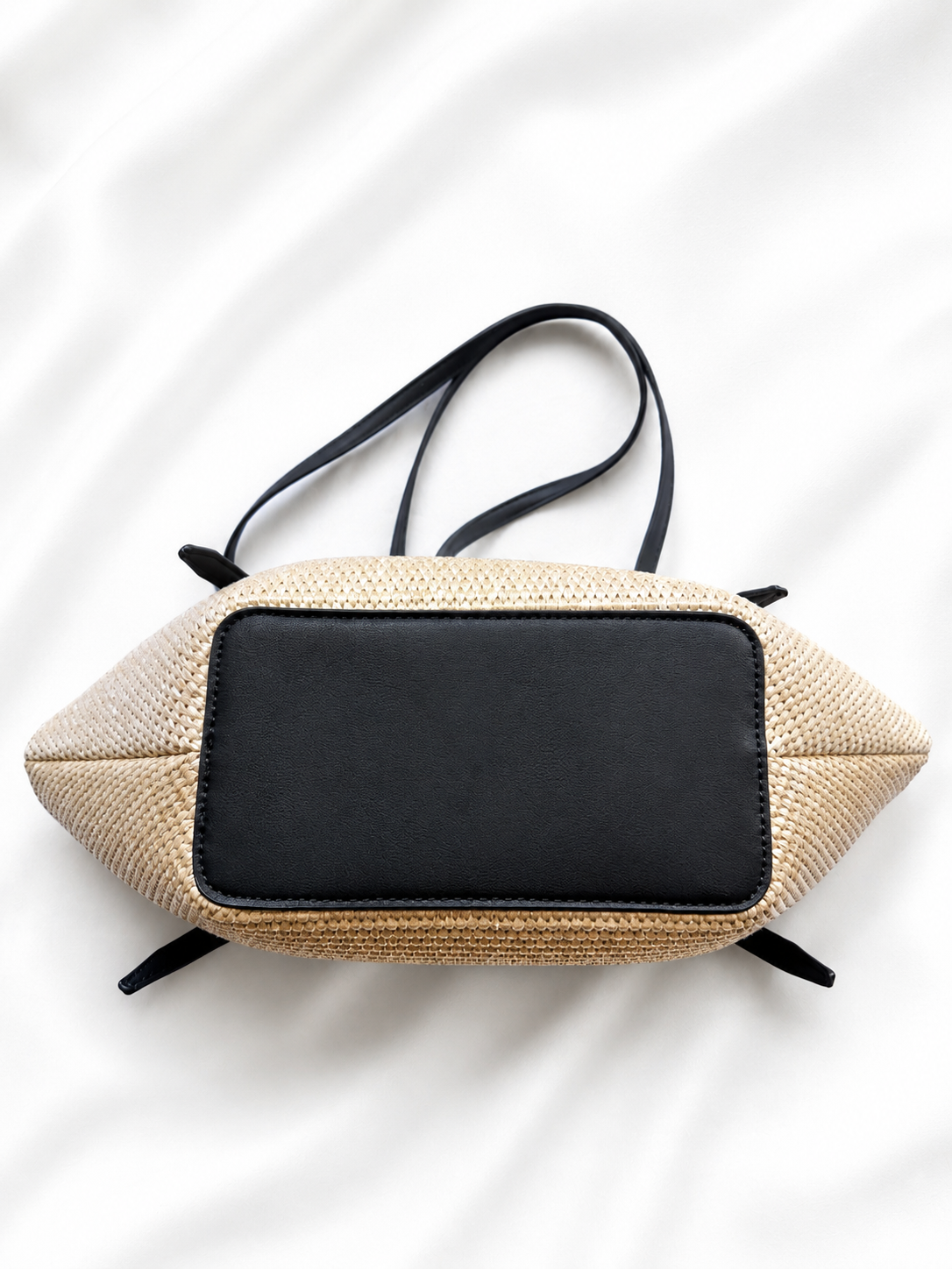 Beige woven handbag with a black flap on a white background