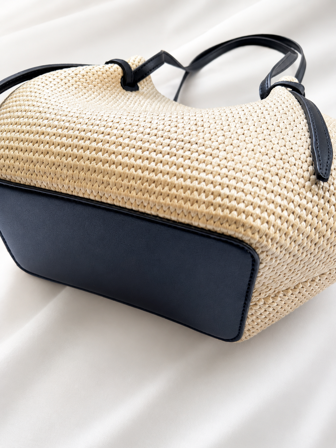 Beige woven handbag with black leather accents on a white background