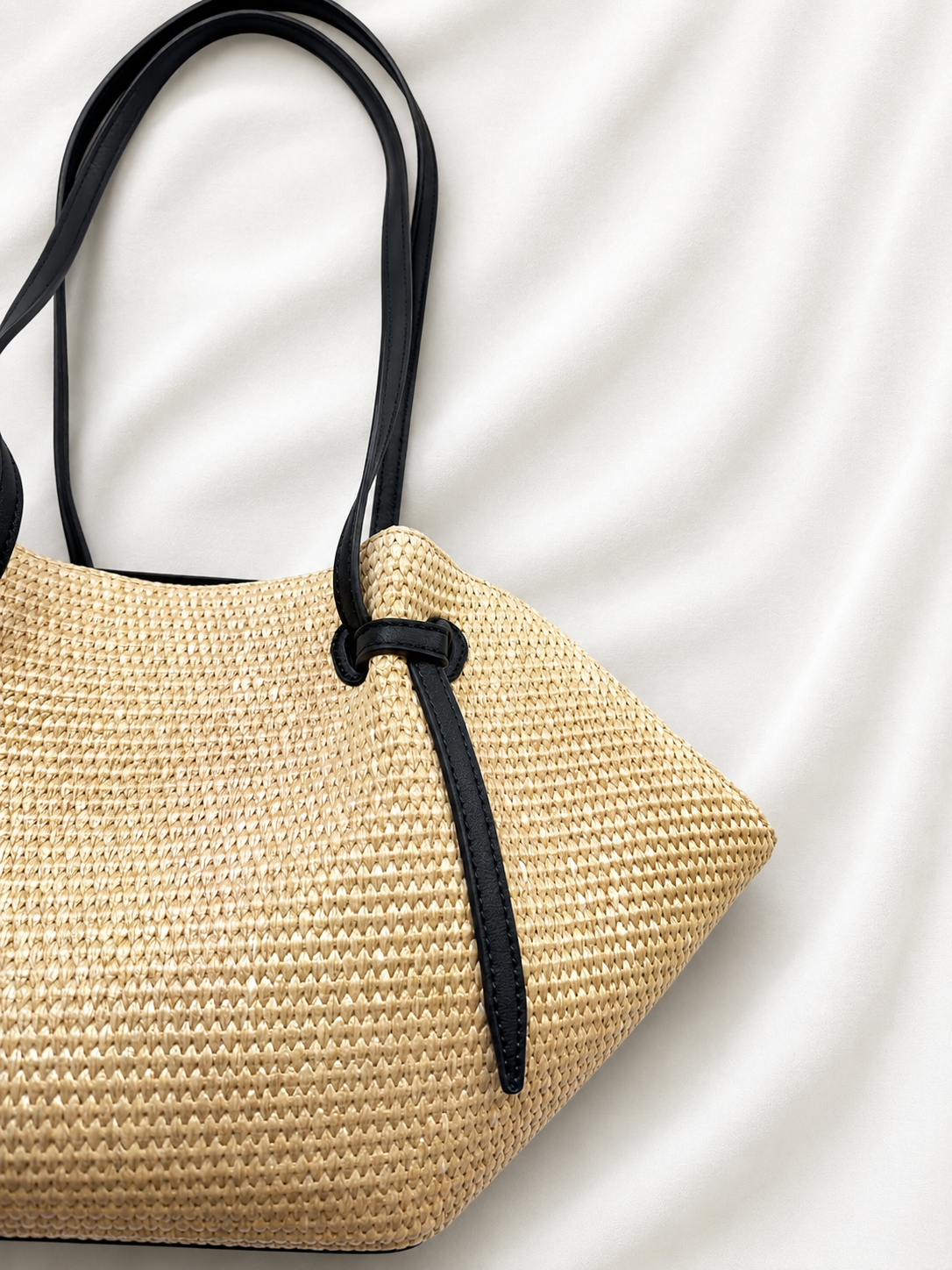 Woven straw handbag with black handle on a light background