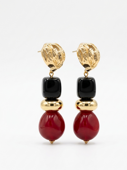 Pair of earrings with gold tops, black beads, and red stones on a white background