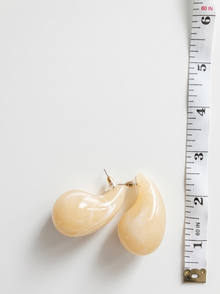 Pair of beige earrings next to a measuring tape on a white background